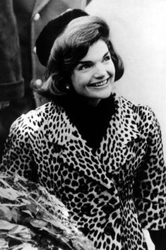 an old photo of a woman wearing a leopard print coat and hat smiling at the camera