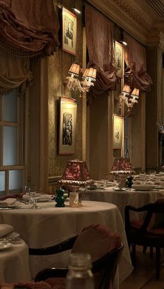 a dining room with tables and chairs covered in white tablecloths, chandeliers and pictures on the wall