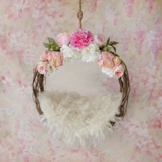 a floral wreath hanging from a rope on a pink wallpapered background with white and pink flowers