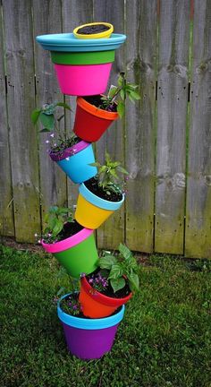 a stack of colorful pots with plants growing out of them on the grass in front of a fence