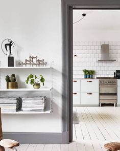 a kitchen with white walls and flooring has plants on the shelves above the stove