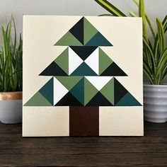 a green and white christmas tree on a wooden table next to potted plantes