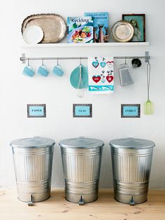 three metal trash cans sitting on top of a wooden floor next to a white wall