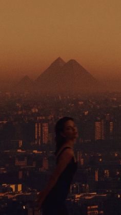 a man standing on top of a tall building next to a city skyline at sunset