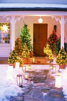 lighted christmas trees in front of a house with snow on the ground and lit candles