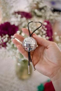 a person holding a small disco ball on a black cord with flowers in the background