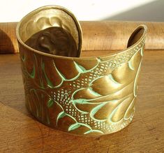 a gold colored cuff bracelet with green and white designs on the inside, sitting on a wooden surface