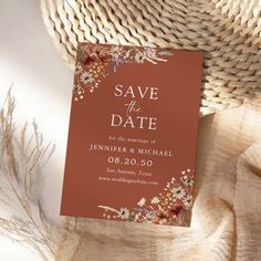 an orange save the date card sitting on top of a white cloth next to a straw hat