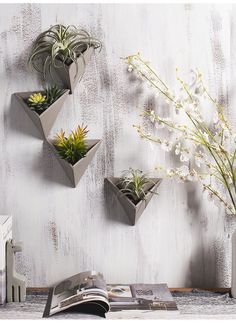 three planters are hanging on the wall above a book and vase with flowers in it