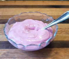 a bowl filled with pink colored food on top of a wooden table next to a spoon