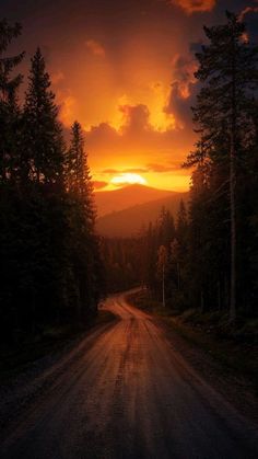 the sun is setting over a dirt road with trees on both sides and mountains in the distance