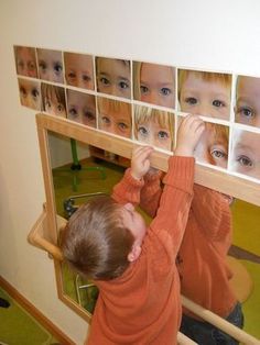 a young boy looking at his own faces in a mirror with pictures on the wall