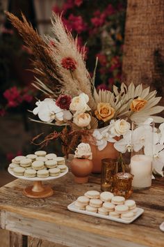 an arrangement of flowers and desserts on a wooden table with white frosted donuts