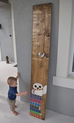 a little boy standing next to a wooden growth chart