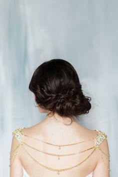 the back of a woman's dress with gold chains on her shoulders and shoulder