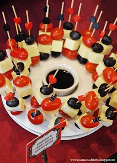 an assortment of cheese and tomato skewers arranged on a white plate with black sauce