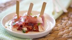 small white bowl filled with food and toothpicks on top of a woven table cloth