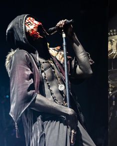 a man in a black outfit holding a microphone and wearing a mask on his face