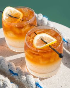 two glasses filled with drinks sitting on top of a white table next to a rope