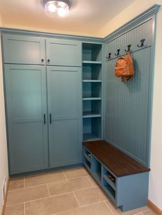 a room with blue cabinets and a bench in the center, two bags hanging from hooks on the wall