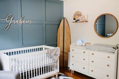 a baby's room with a surfboard, dresser and crib in it