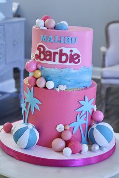 a pink and blue cake with palm trees on it's side, sitting on top of a table