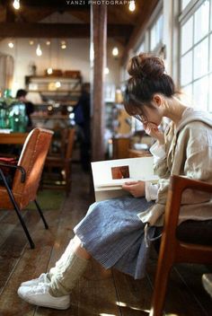 a woman sitting at a table with a book in front of her and looking down