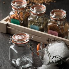 salt and pepper shakers in glass jars on a wooden tray with spices scattered around them