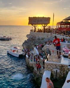 people are standing on the edge of a cliff by the water at sunset or sunrise