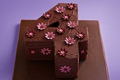 a chocolate cake with pink flowers on it sitting on a purple plate against a purple background