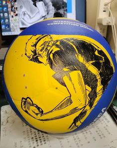 a yellow and blue ball with a drawing of a man on it sitting on top of a table