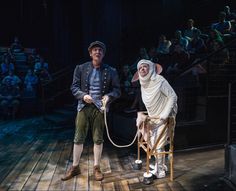 two actors dressed in period costumes on stage with audience watching them from the stands and holding ropes