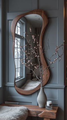 a vase with flowers in it sitting next to a mirror on the wall above a table