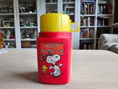 a red and yellow cup sitting on top of a table next to a book shelf