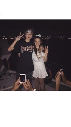 two people standing next to each other on a boat at night with their hands in the air