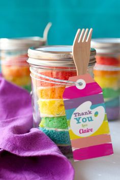 a jar filled with rainbow colored cake next to a purple towel and wooden utensils