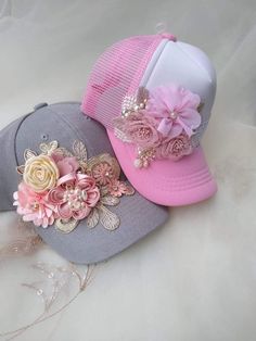 two hats with flowers and pearls on the brim, one in grey and one in pink