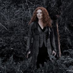 a woman with red hair standing in the woods