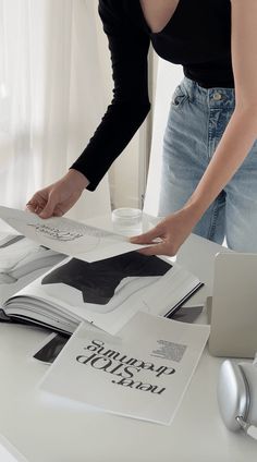 a woman standing over a table with books on top of it and an open book in front of her