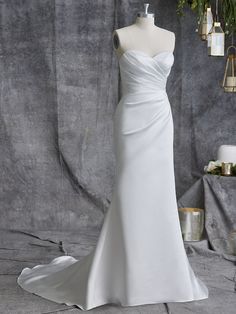 a white wedding dress on display in front of a gray backdrop with greenery and candles