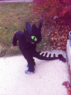 a little boy dressed up as a black cat with green eyes standing on the sidewalk