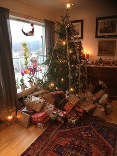 a christmas tree with presents under it in a living room next to a large window