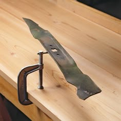 a knife is attached to a piece of metal on a wooden table top with a wrench