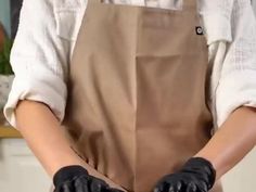 a woman wearing black gloves is making something with her hands in the air and holding on to an apron