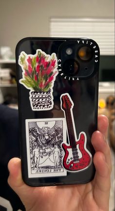 a person holding up a phone case with stickers on it and a flower in a pot