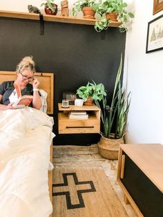 a woman laying in bed reading a book with plants on the shelves above her head