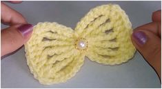 a crocheted yellow bow with a pearl in the center is being held by someone's hand