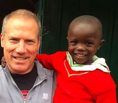 an older man is holding a young boy in front of a green building and smiling at the camera