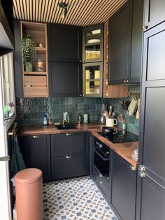 a kitchen with black cabinets and tiled flooring in the center, along with an orange trash can