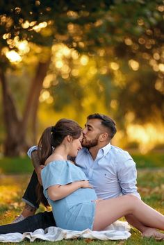 a man and woman sitting on the grass in front of trees with their backs to each other